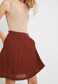Beige ribbad linnepar med en rostfärgad knälång kjol som har elastisk midja och sidofickor, tillverkad av lätta material.