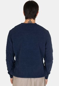 Maglione blu scuro con un motivo testurizzato sulle maniche e sul retro. Collo rotondo, polsini e orlo a coste. Tessuto lavorato morbido.