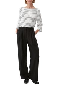 Blusa bianca con strisce nere, scollatura a barca e maniche a tre quarti; abbinata a pantaloni neri a vita alta, plissettati e scarpe nere.