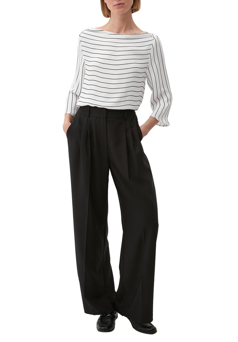 Blusa bianca con strisce nere, scollatura a barca e maniche a tre quarti; abbinata a pantaloni neri a vita alta, plissettati e scarpe nere.