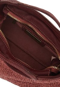 Interno di una borsa intrecciata color bordeaux con fodera marrone, caratterizzata da una cerniera e un'etichetta dorate. Materiale strutturato e tasche interne visibili.