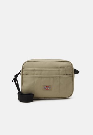 Bolsa rectangular verde oliva de tejido duradero, con un parche de logo, dos bolsillos frontales y una correa negra desmontable.