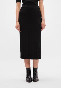 Fustă midi din tricot negru cu nervuri, cu talie ajustată și textură verticală, asociată cu botine negre. Design simplu și versatil.