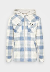 Veste à capuche zippée avec capuche gris clair, tissu polaire à carreaux bleu et blanc, et deux poches poitrine avec rabats à boutons.