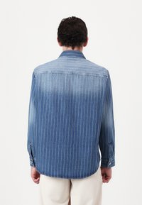 Denim shirt with vertical white stripes, button cuffs, and a back yoke. Fabric has a medium texture and a gradient from dark to light blue.