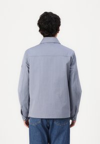 Lys grå langermet skjorte med krage, som har et enkelt design, glatt tekstur og knappede mansjetter. Brukt med blå jeans.