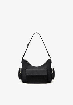 Čierna kabelka na rameno s hlavným priehradkom na zips, dvoma bočnými priehradkami na zips a predným vreckom s chlopňou na bielom pozadí.