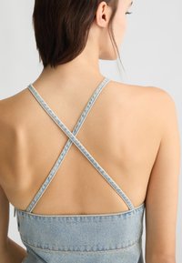Vestito in denim con spalline incrociate e corpino aderente. Tessuto azzurro chiaro con una trama liscia e design minimalista sul retro.