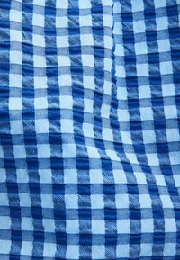 Tissu à carreaux bleu et blanc avec une texture tissée ; présente des carrés alternés de bleu uni et de bleu clair, créant un motif en grille.