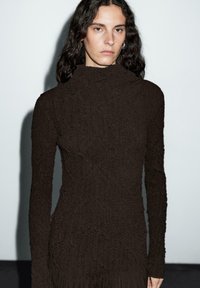 Black long-sleeve turtleneck top, textured fabric with a wavy pattern, fitted design, and a high neckline. Minimalist aesthetic.