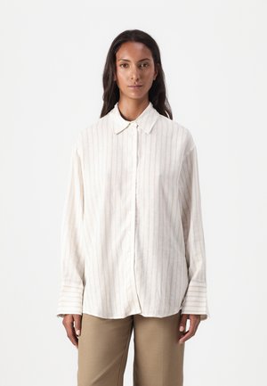 Hvit skjorte med lyse beige vertikale striper, klassisk krage og brede mansjetter. Kombinert med lysebrune bukser.
