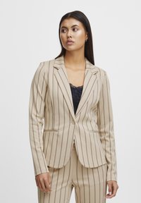 Beige gestreifter Blazer mit taillierter Passform, der vertikale braune Linien, Revers und eine Ein-Knopf-Verschluss aufweist. Texturiert Stoff.