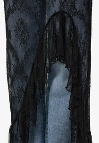 Černá krajka s květinovými vzory překrývá modrý denim. Krajka má nařasené okraje, které dodávají texturu a detaily.