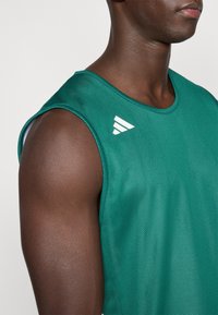 Green mesh athletic tank top with rounded neckline, sleeveless design, and a white logo accent on the shoulder. Smooth texture.