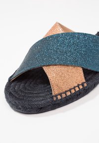 Třpytivý tyrkysový a bronzový design s křížovými pásky na černé pletené jutové podešvi. Má texturovan ý svršek a prošívaný detail podél okraje.