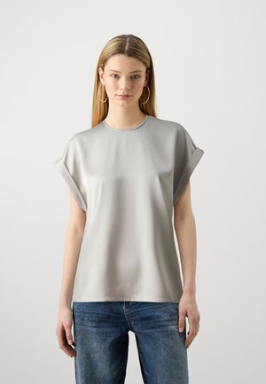Maglietta grigia chiara a maniche corte con una texture liscia e lucida e risvolti, abbinata a jeans di denim blu chiaro.