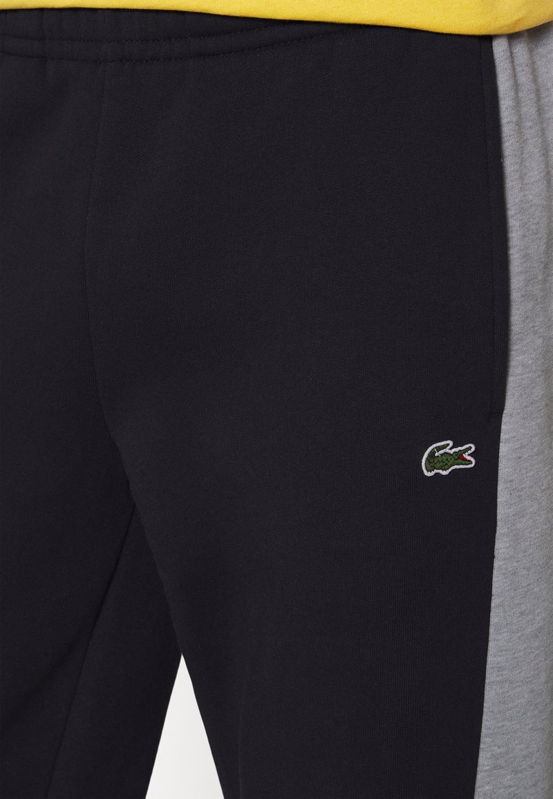 Pantalons de survêtement noirs et gris en coton avec une texture lisse, arborant un petit logo crocodile vert brodé sur la jambe inférieure.