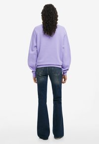 Paarse hoodie met een relaxed fit en ribgebreide manchetten, gecombineerd met donkerblauwe, uitlopende jeans met achterzakken en een versleten textuur.