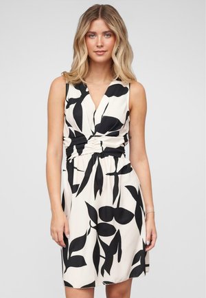 Robe sans manches en tissu crème avec un motif de feuilles noires, décolleté en V, taille froncée et coupe décontractée qui tombe au-dessus des genoux.