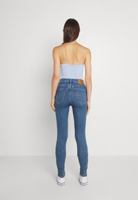 Vaqueros ajustados de mezclilla azul medio, de tiro alto, con parche de cuero en la parte trasera, dos bolsillos traseros y un ajuste ceñido en los tobillos.