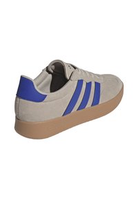 Sneaker in suede grigio chiaro con strisce blu, forma arrotondata e suola in gomma beige. Presenta lacci e dettaglio del logo sul tallone.