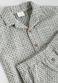 Leichte, gemusterte Baumwollbluse mit Kragen, braunen Holzknöpfen und einer Vordertasche; hat ein geometrisches Design in Schwarz und Weiß.