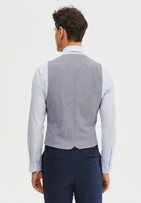 Szary kamizelka w kratkę o eleganckim kroju, noszona na jasnoniebieskiej koszuli, z dopasowanym krojem i rozcięciem z tyłu dla lepszej struktury.