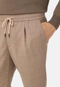 Béžové, strukturované kalhoty s elastickým pasem a šňůrkou na stažení. Obsahují boční kapsy a jemné přední záhyby.