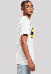 White cotton t-shirt featuring a large black and yellow Batman logo on the front, with short sleeves and a classic crew neck design.