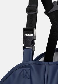 Gros plan d'une sangle noire ajustable avec boucle en plastique fixée à un sac ou vêtement en tissu bleu étanche.