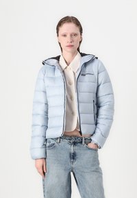 Lys blå dunjakke med hette, har glidelåsforsiden, svart trim og diskret merke. Teksturert, kviltet design med cropped snitt.