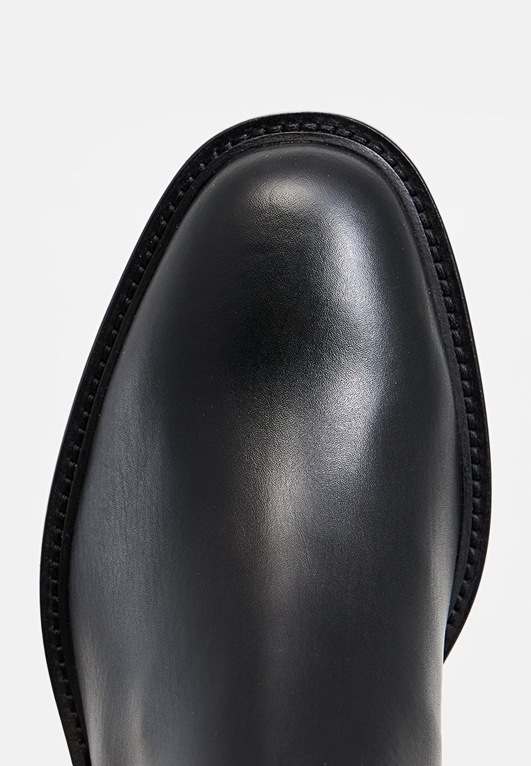 Schwarzer Lederschuh mit runder Zehenform, glatter Textur und kontrastierenden Nähten entlang des Randes, der ein schlankes und modernes Design präsentiert.