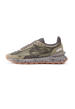 Vista lateral de un zapato deportivo verde oliva con suela estampada, cordones grises, detalles en ante y un pequeño logo en el talón.
