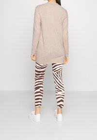 Světlý béžový svetr s dlouhým rukávem, zkombinovaný s dobře padnoucími legínami se zebra vzorem v bílé a tmavě hnědé barvě a bílými sneakers. Měkká textura, casual styl.