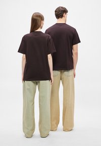 Brązowe bawełniane koszulki z krótkim rękawem, połączone z luźnymi, wysokim stanem spodniami w jasnej zieleni i beżu. Minimalistyczny design, bez widocznych logo.