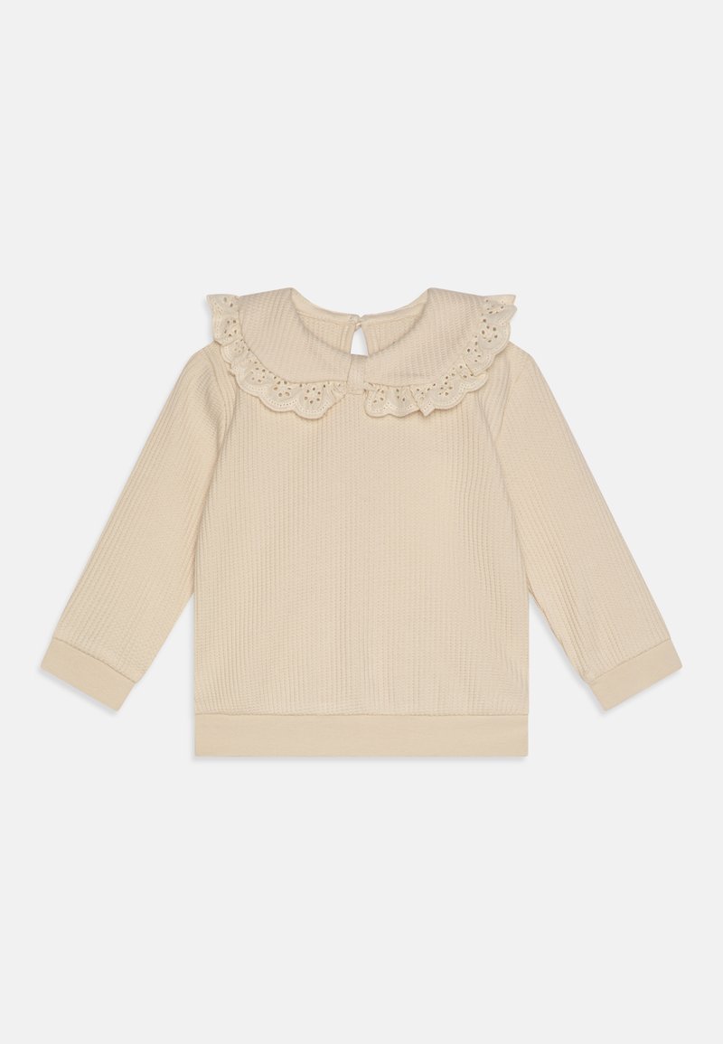 Top de manga larga beige con textura acanalada, cuello con encaje y cierre en forma de clave en la parte posterior. Las muñecas y el dobladillo ajustados completan el diseño.