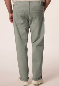 Vihreät puuvillapuvut suoralinjaisella leikkauksella, joissa on takataskut ja huomaamattomat ompelutiedot. Yhdistetty valkoisiin lenkkareihin.