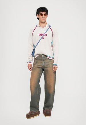 White knit sweater with "BONSAI 10" in red, blue accents. Wide, faded brown jeans. Brown embroidered shoes, tinted sunglasses, and crossbody bag.