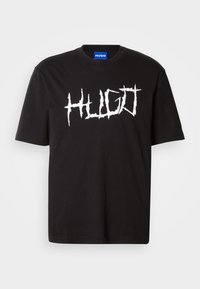 Μαύρο βαμβακερό t-shirt με στρογγυλή λαιμόκοψη και κοντά μανίκια, διαθέτοντας έναν έντονο λευκό γραφικό λογότυπο "HUGO" σε αγκαθωτή γραμματοσειρά.