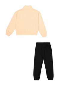Chaqueta de cremallera color durazno claro con cuello alto y dobladillo elástico, combinada con pantalones de chándal negros con cintura elástica y tobillos acampanados.
