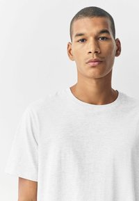 Vit kortärmad t-shirt gjord av lättviktig tyg, med rund halsringning och en mjuk, något strukturerad yta.
