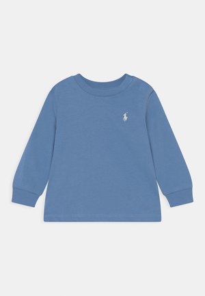 Blå babybluse med lange ærmer, rund halsudskæring, to trykknapper på den ene skulder og hvidt broderet logo på brystet.