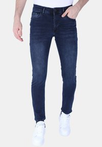 Donkerblauwe denim jeans voor heren met een slim fit, klassiek vijf-pocket ontwerp en subtiele vervaging. Gestyled met witte sneakers.