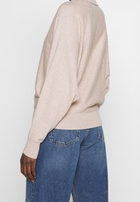 Maglione beige lavorato a maglia con vestibilità comoda, polsini e orlo a coste; abbinato a jeans in denim lavaggio medio con tasche posteriori.