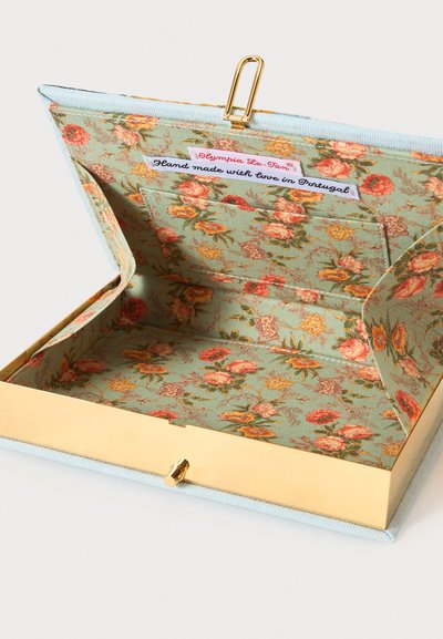 Pochette en tissu à motif floral ouverte, avec cadre métallique doré et étiquette portant l'inscription "Hand made with love in Portugal."