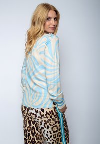 Lange mouwen blouse in licht crème met abstract blauw patroon. Gecombineerd met leopardprint broek met een turquoise zijstreep. Zachte textuur.