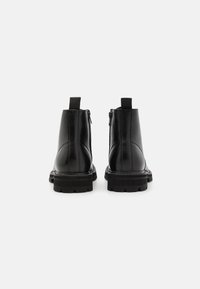 Paire de bottines en cuir noir à semelles épaisses vues de dos sur un fond clair uni.