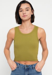 Λαδί πράσινο ριμπ τοπ χωρίς μανίκια με στρογγυλή λαιμόκοψη, κομμένο ύψος, συνδυασμένο με τζιν παντελόνι υψηλής μέσης.