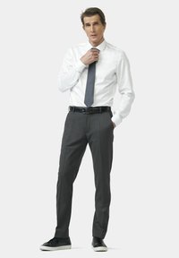 Chemise blanche à bouton, pantalon gris foncé et baskets noires. La chemise a des manches longues ; le pantalon est ajusté avec une texture lisse et une ceinture.