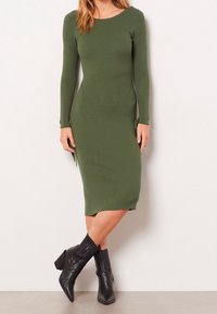 Ribbad långärmad klänning i olivgrön, figurnära design, knälång. Matcher med svarta, klackiga ankelstövlar med texturerade detaljer.